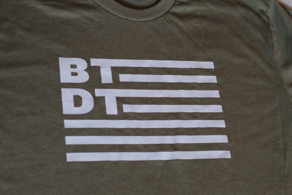 Our classic T-shirt with flag logo. Olive green shirt with white ink 